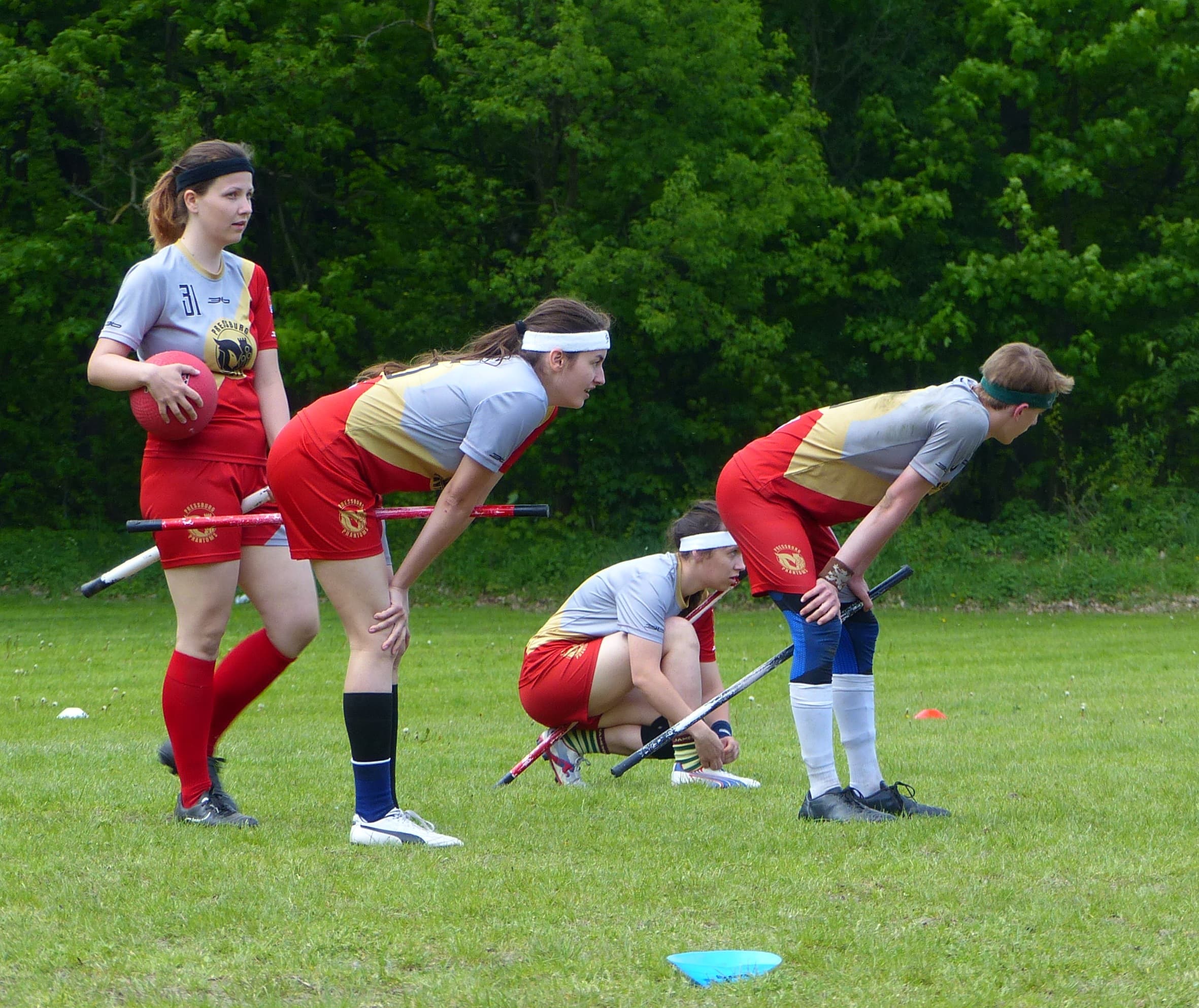Quadball players line up on a grass field with balls and broomsticks
